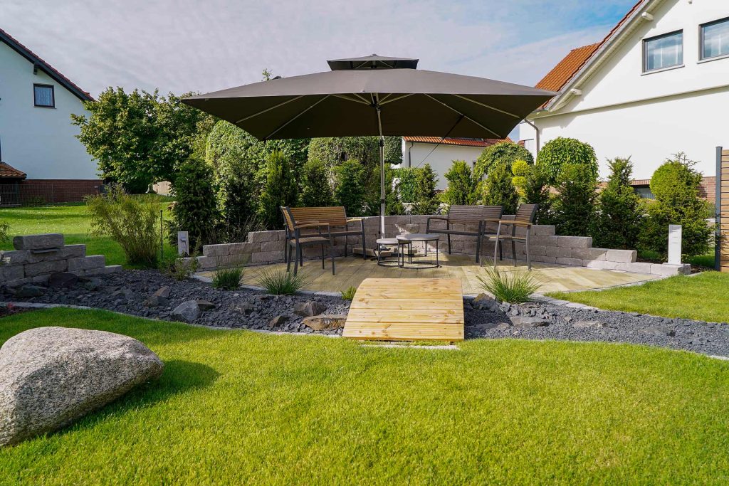 Gartengestaltung mit Sitzbereich, Sonnenschirm und Brücke, erstellt von der Firma Aussengestaltung Vogt