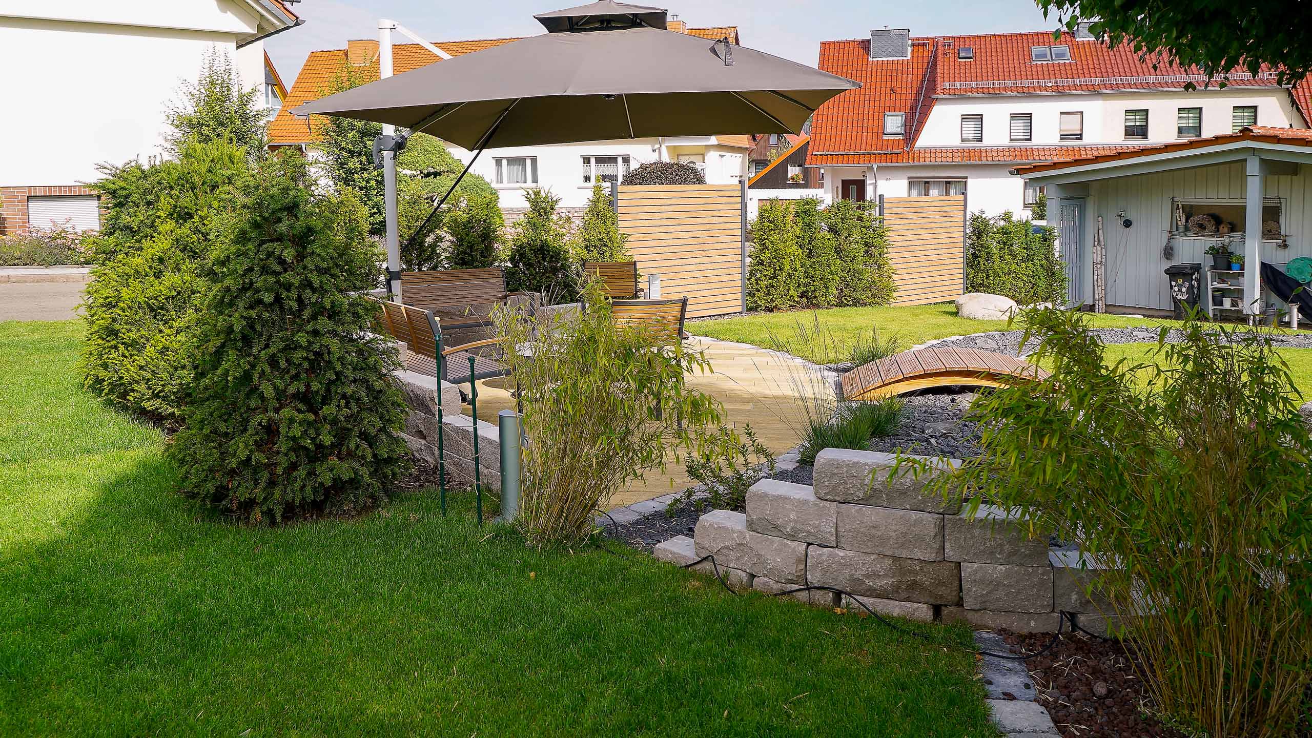 Gartengestaltung mit Sitzbereich, Sonnenschirm und Brücke, erstellt von der Firma Aussengestaltung Vogt