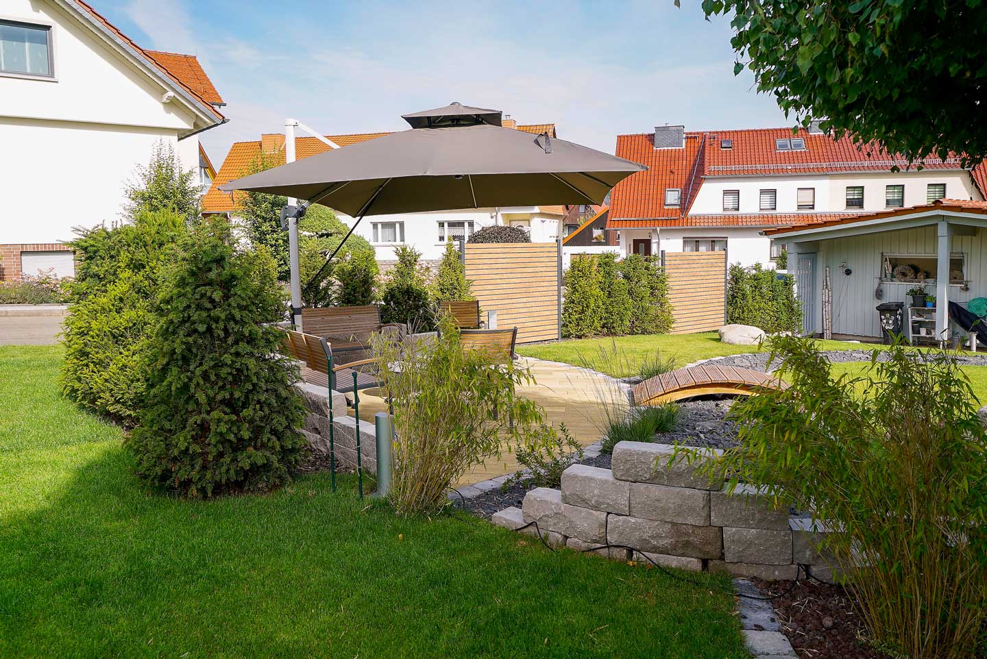 Gartengestaltung mit Sitzbereich, Sonnenschirm und Brücke, erstellt von der Firma Aussengestaltung Vogt
