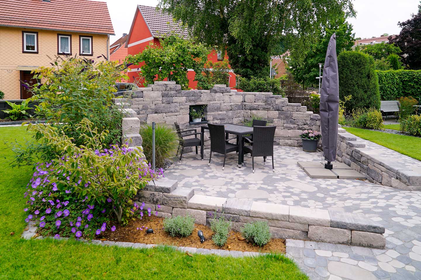 Gartengestaltung mit gepflasterter Sitzecke und Sonnenschirm, erstellt von der Firma Aussengestaltung Vogt